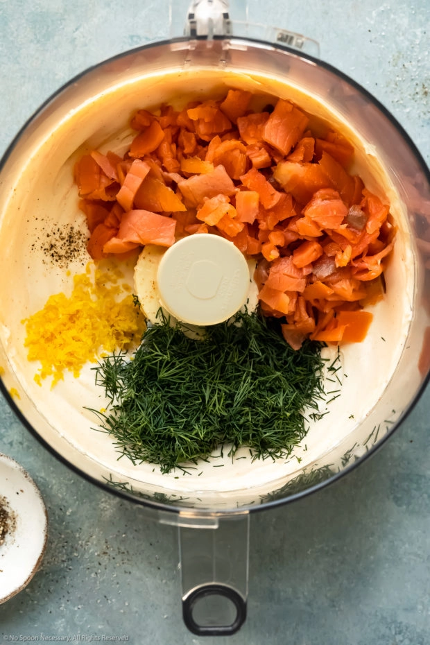 Overhead photo of a food processor bowl filled with whipped cream cheese, smoked salmon, lemon zest, fresh dill and cracked black pepper - photo of step 2 of the recipe.