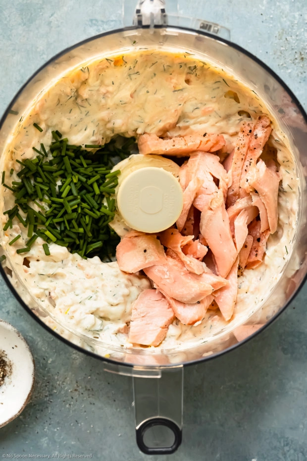 Overhead photo of a food processor bowl filled with smoked salmon whipped cream cheese and topped with flaked wild salmon and chives - photo of step 3 of the recipe.