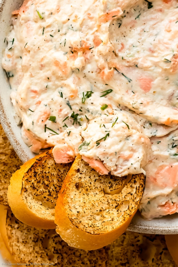 Overhead, close-up photo of two slices of toasted baguette dipped into salmon spread.