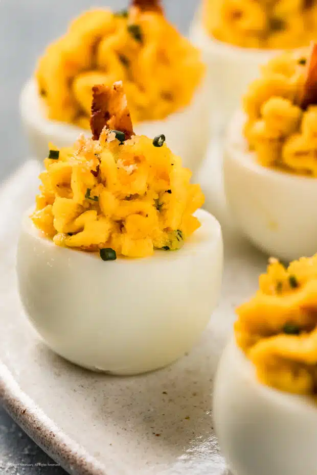 Angled photo of a bacon deviled egg garnished with a crispy piece of bacon.