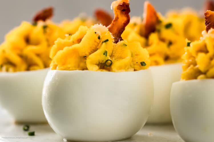 Straight on photo of a standing up devilled eggs with bacon on a white kitchen tray.