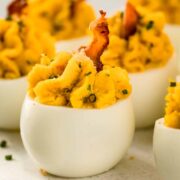 Straight on photo of a seven deviled eggs with bacon on a white serving platter.