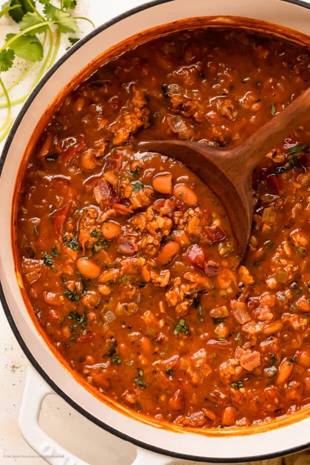 Overhead photo of cooked charros beans recipe in a large white pot with a wooden spoon.