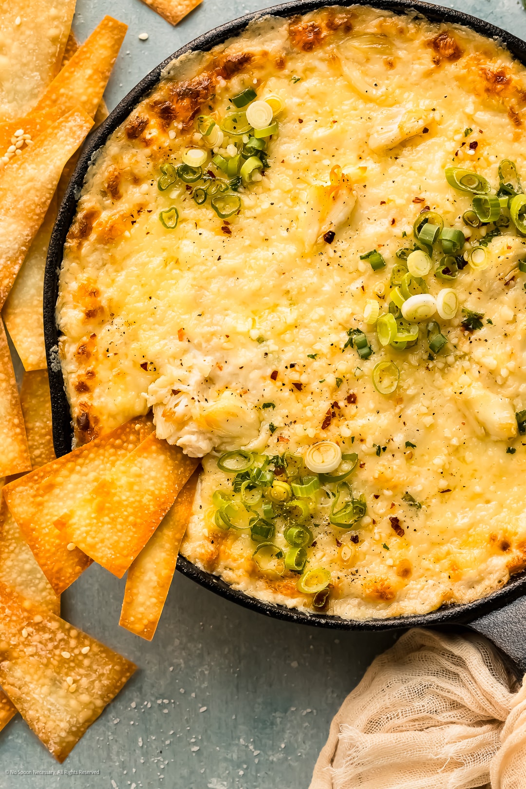 Overhead photo of a crispy baked wonton chip inserted into a skillet of crab dip.
