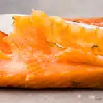 Close-up action photo of gravlax being sliced with a sharp knife.