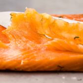 Close-up action photo of gravlax being sliced with a sharp knife.