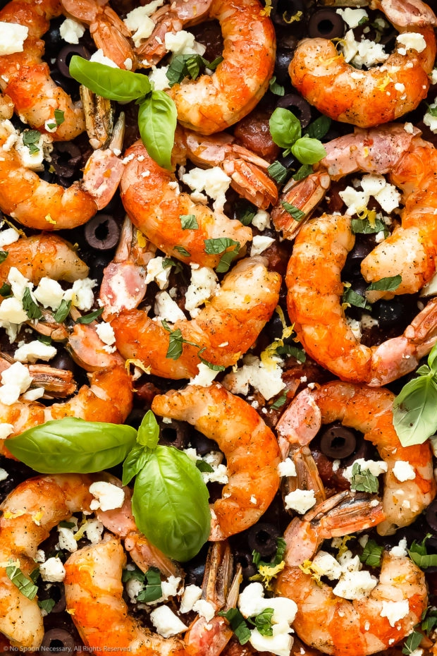 Overhead, close-up photo of Greek baked shrimp with tomatoes, feta, olives and fresh basil.