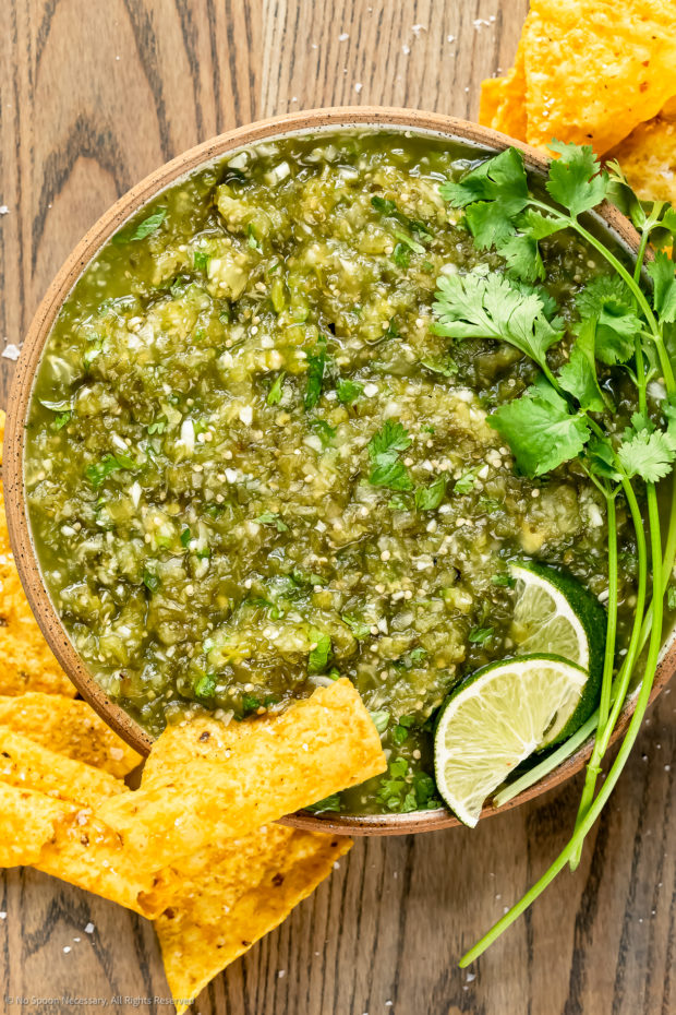 Overhead photo of chunky green salsa in a serving bowl with a yellow tortilla chip inserted into the salsa. 