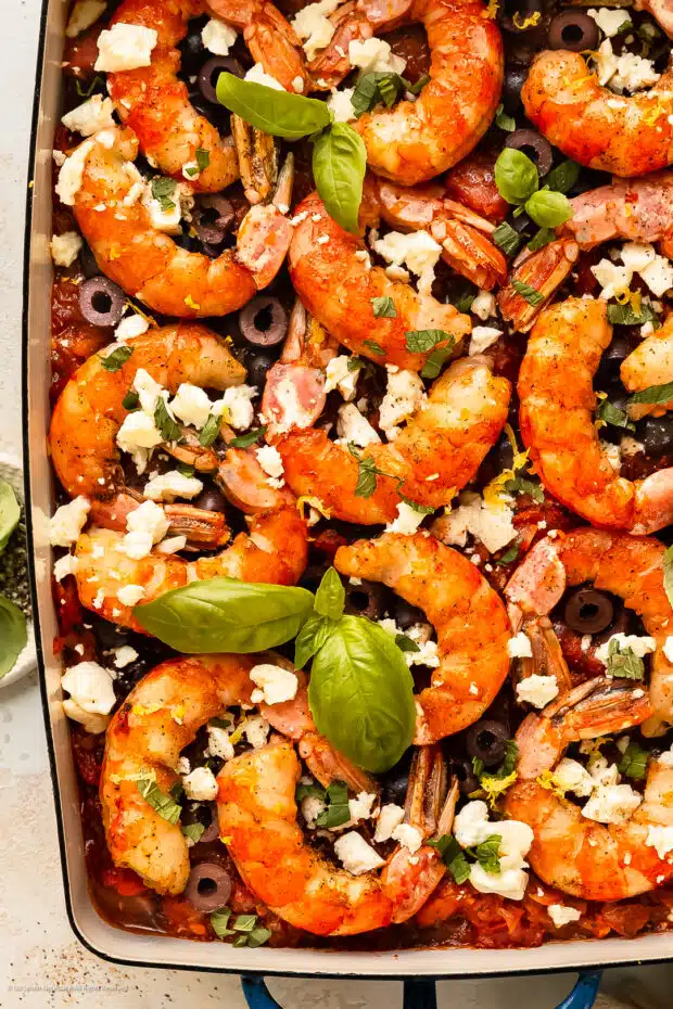 Overhead photo of cooked greek shrimp with feta cheese, tomatoes, and seasonings in a baking dish.