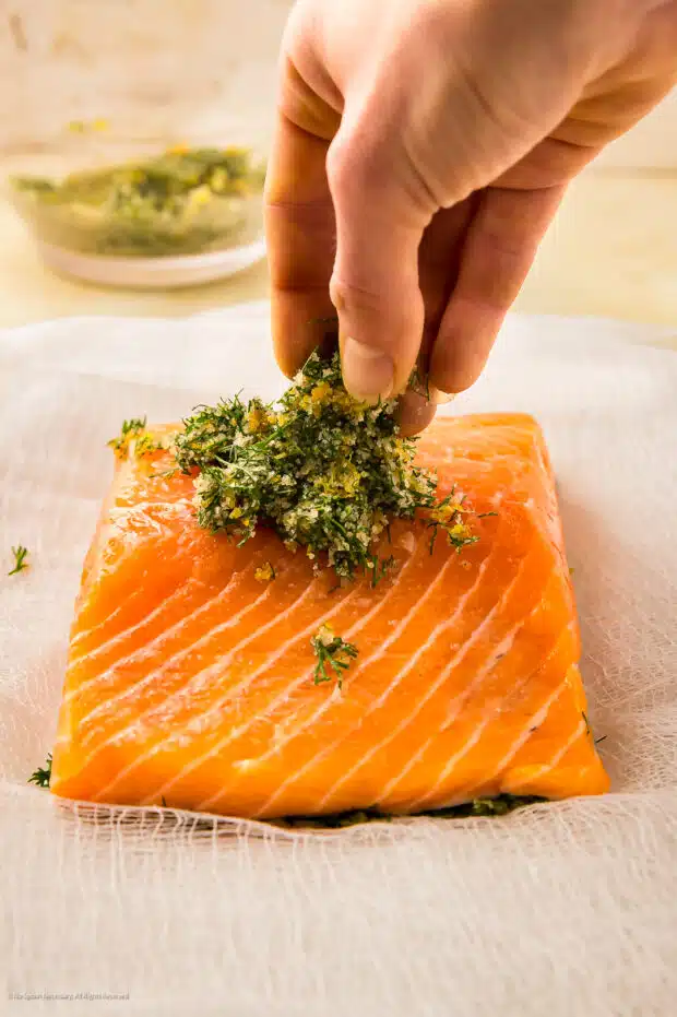 Straight on action photo of a person applying a cure to a raw salmon filet.