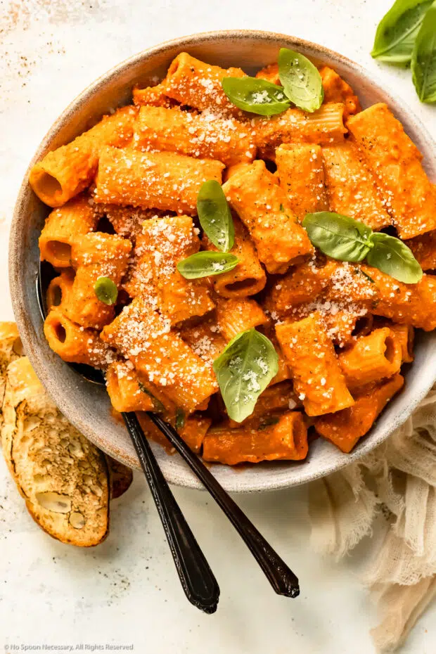 Overhead photo of roasted red pepper pasta with fresh basil in a serving bowl.
