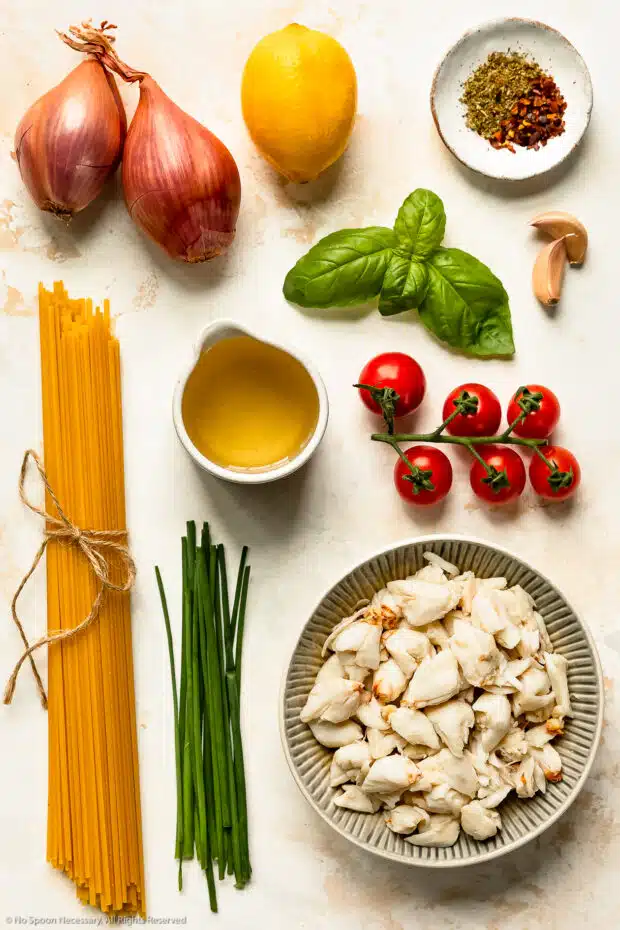 Overhead photo of all the ingredients needed to make crab linguine recipe neatly organized by individual ingredient on a white wood surface.