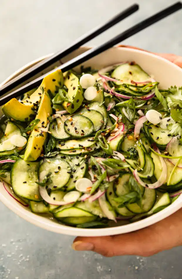 Angled photo of a person holding a bowl of prepared Asian cucumber salad recipe.