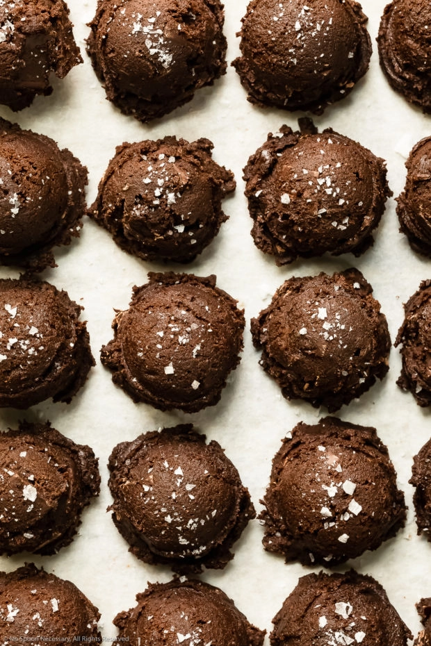 Overhead, close-up photo of raw triple chocolate cookie dough balls sprinkled with flaky salt. 