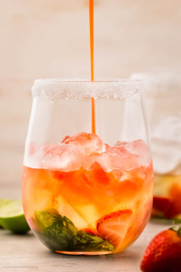 Action photo of a person pouring a cocktail with basil, strawberries and vodka into a drink glass.