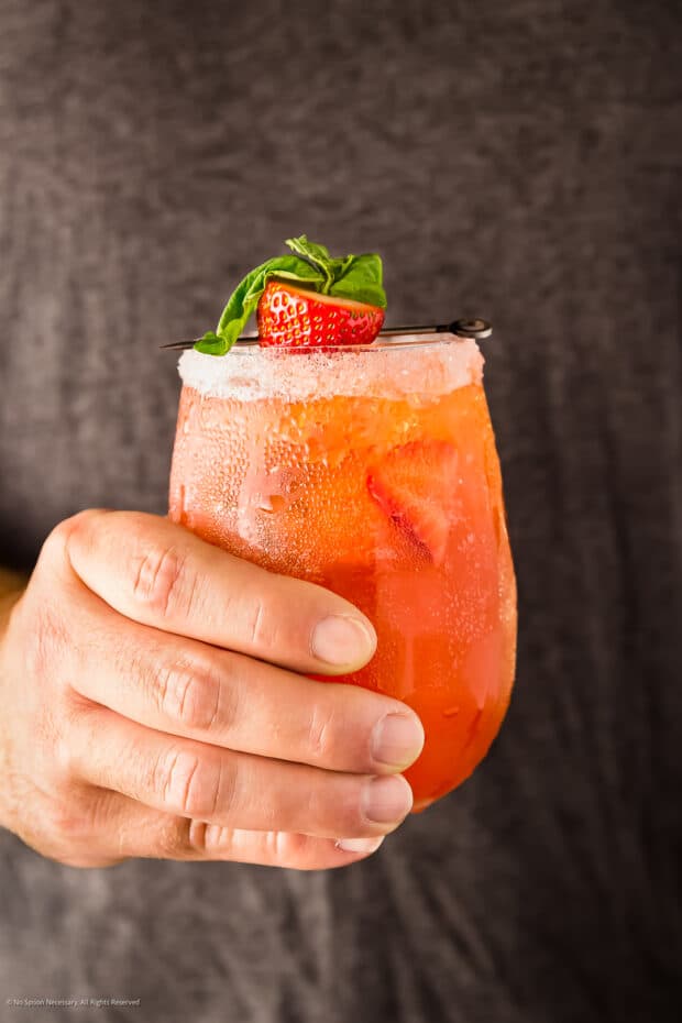 Straight on photo of a hand holding a cocktail with basil.