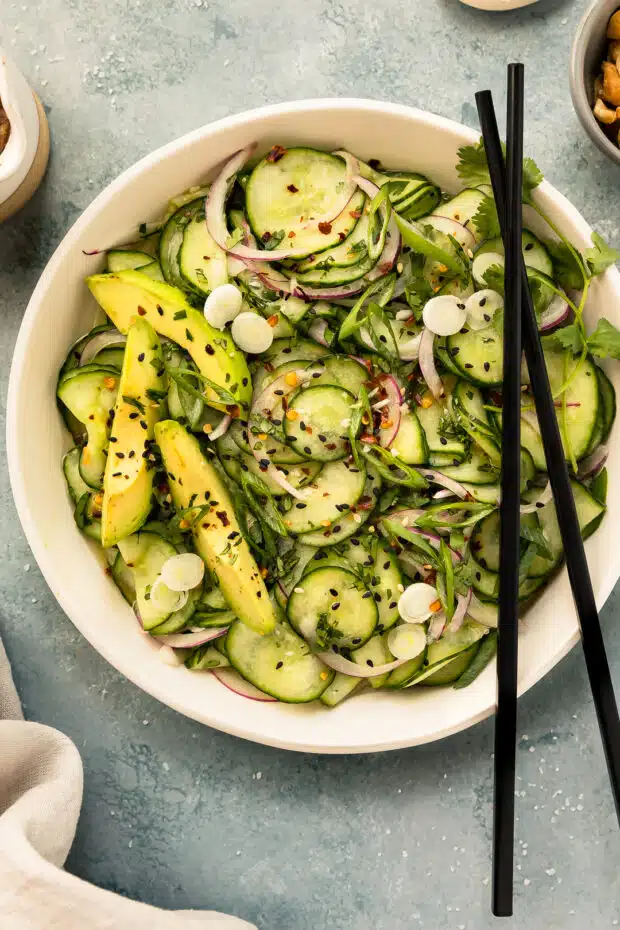 Overhead photo of cucumber salad Asian style in a white bowl with a pair of chopstick resting on the lip of the bowl.