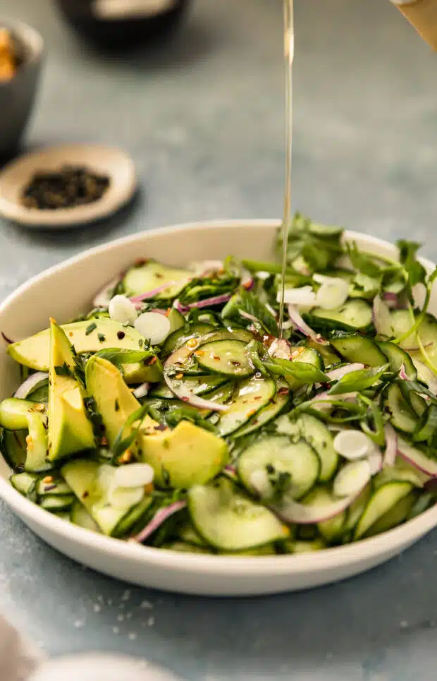 Action photo of rice vinegar being poured over a cucumber salad.