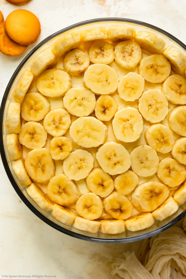 Overhead photo of fresh slices of bananas layered on pudding dessert.