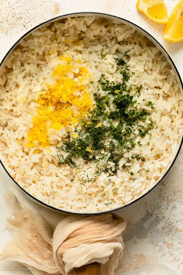 Overhead photo of white greek rice topped with lemon zest and chopped dill fronds in a saucepan.