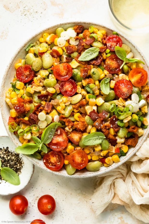 Overhead photo of corn succotash with bacon and tomatoes in a white serving bowl.