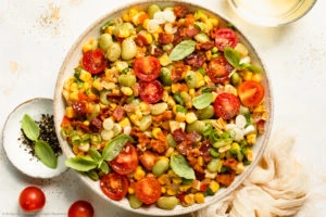 Overhead photo of sweet corn succotash with bacon and tomatoes in a white serving bowl.