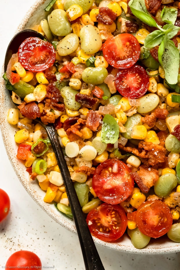 Overhead photo of lima bean and corn salad with bacon and tomatoes in a white bowl with a spoon inserted into the dish.