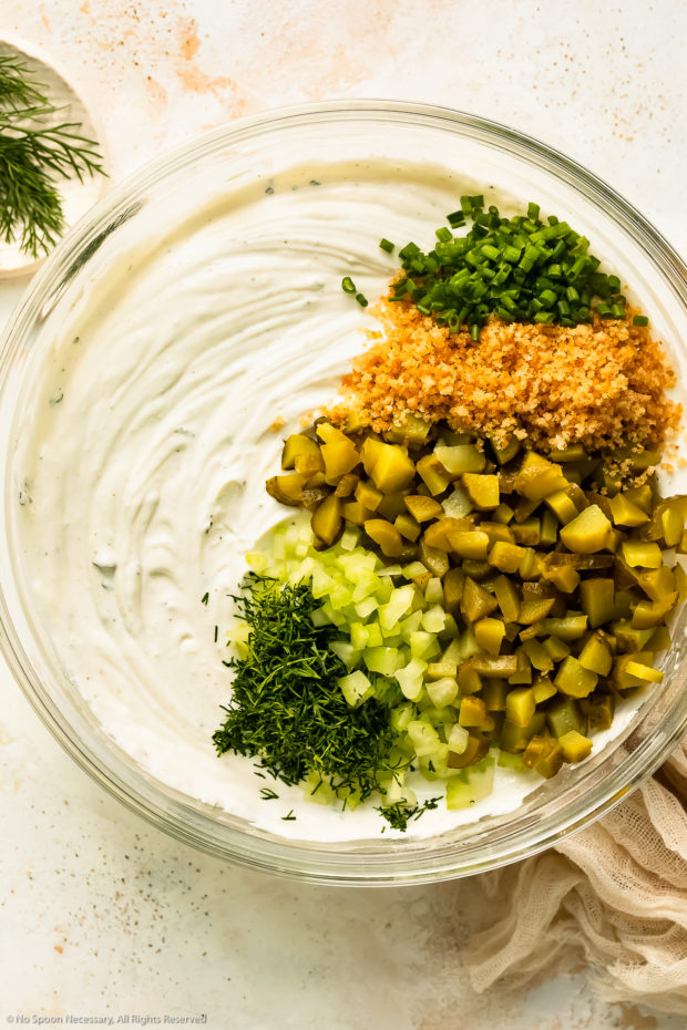 Overhead photo of whipped cream cheese, ranch mix and sour cream topped with chopped dill, diced celery, chopped pickles, breadcrumbs and sliced chives