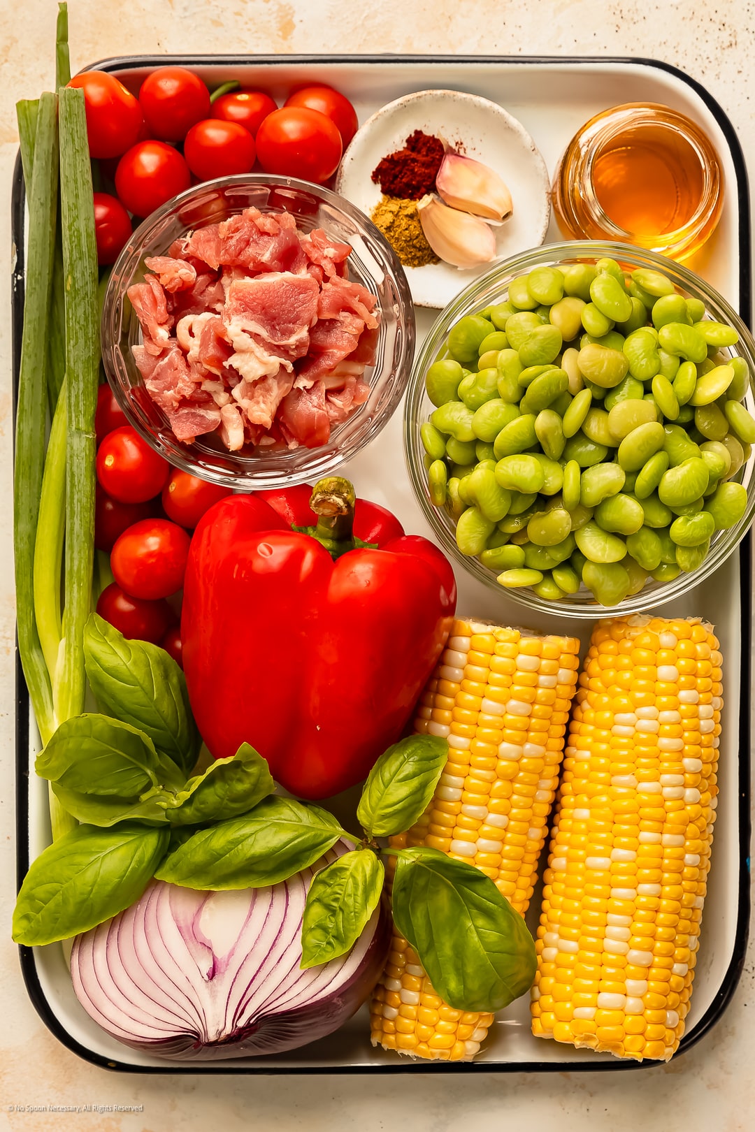 Overhead photo of the ingredients to make succotash - corn, lima beans, tomatoes, bell pepper, onion and fresh herbs - neatly organized on a kitchen tray.
