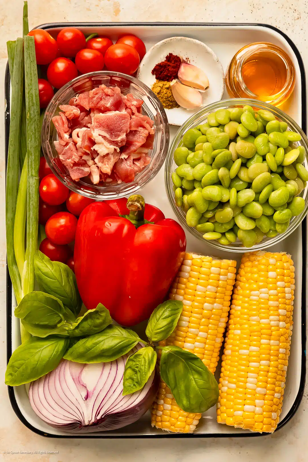 Overhead photo of the ingredients to make succotash - corn, lima beans, tomatoes, bell pepper, onion and fresh herbs - neatly organized on a kitchen tray.