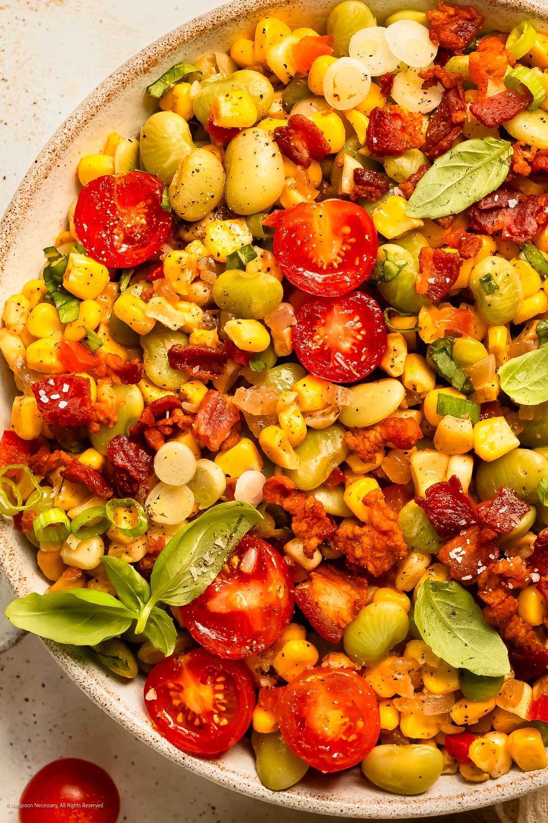 Close-up photo of lima bean and corn succotash with tomatoes in a white serving bowl.