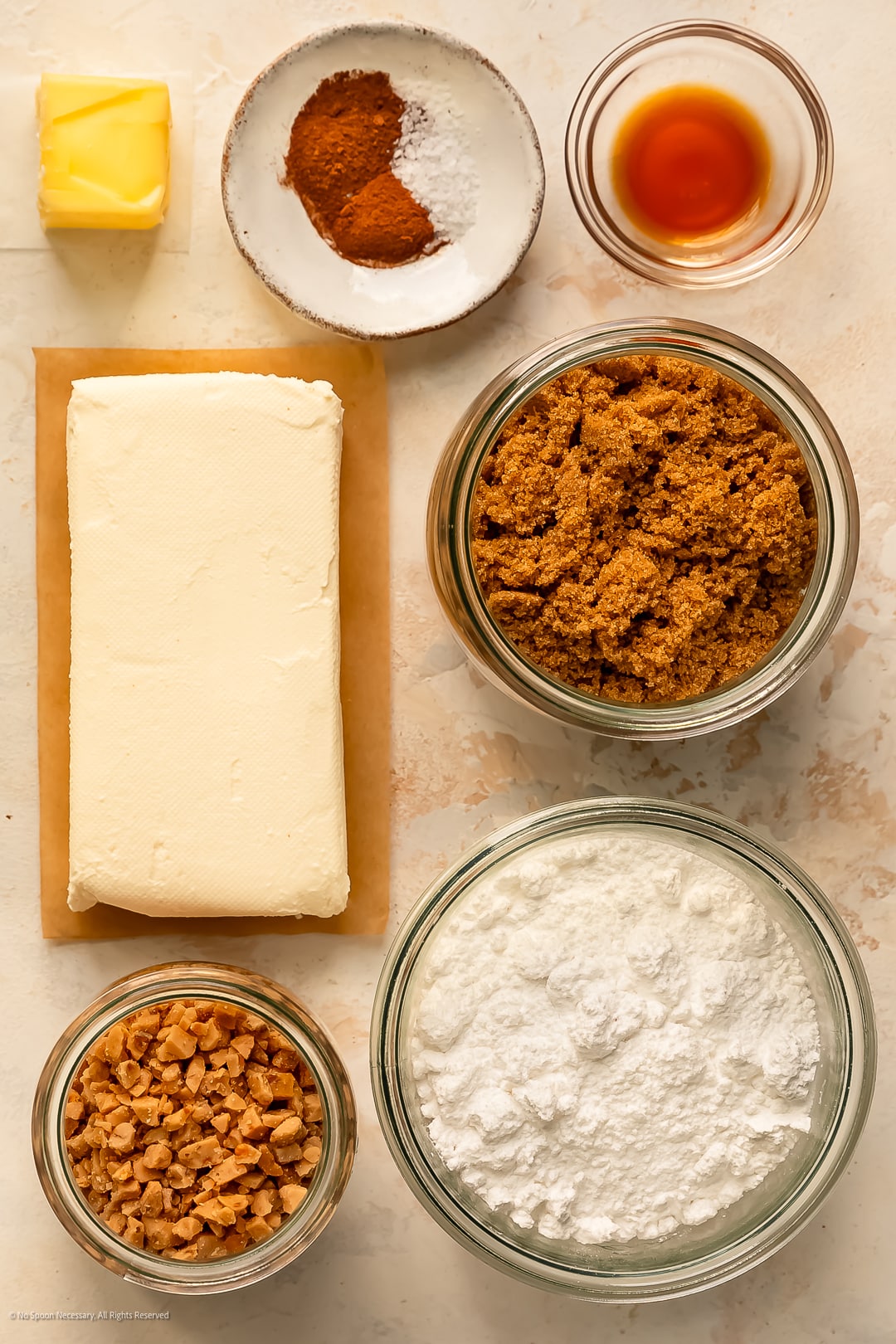 Overhead photo of a block of cream cheese,, brown sugar, confectioner's sugar, vanilla extract, and baking spices neatly arranged on a kitchen counter.