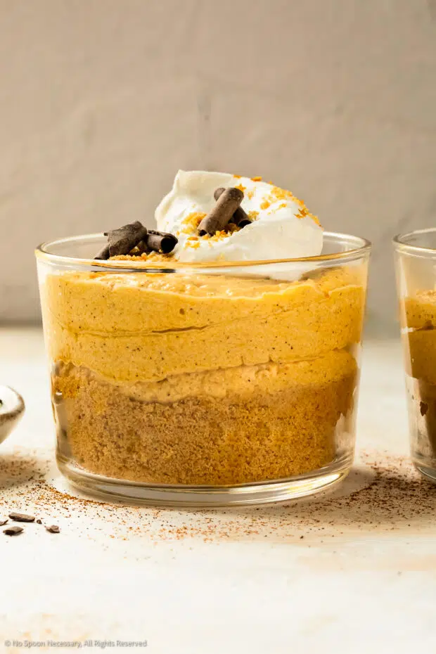 Straight on photo of a parfait glass containing layers of crushed gingersnap cookies, pumpkin mousse and whipped cream.