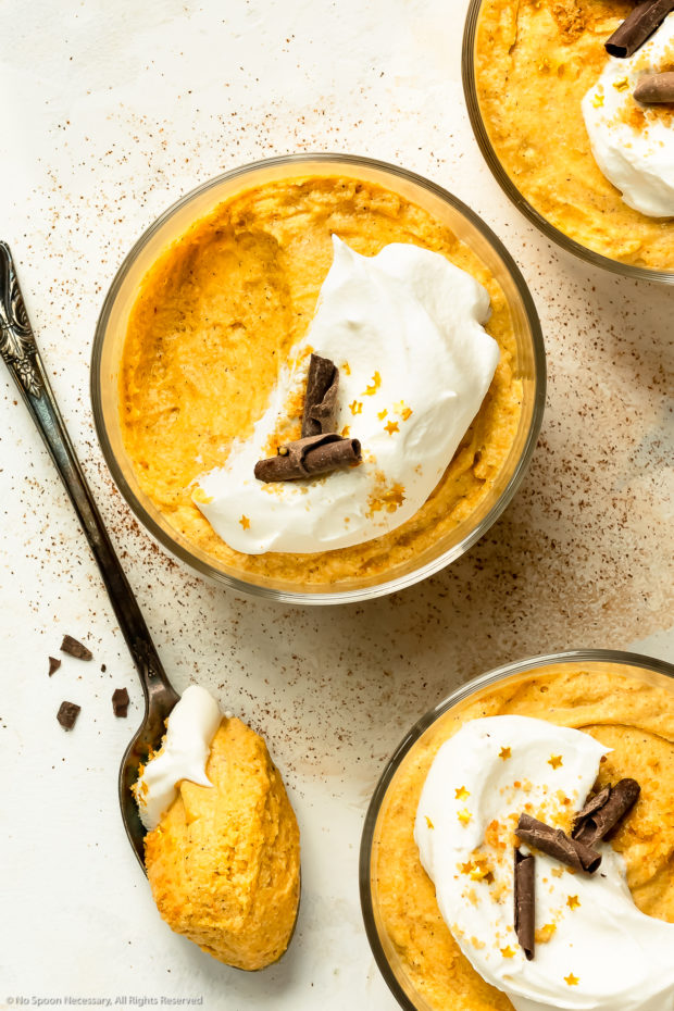 Three short glasses of orange mousse topped with whipped cream and chocolate curls.