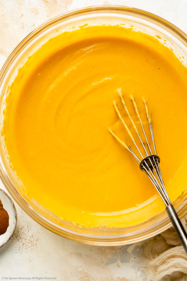 Overhead photo of cream cheese mixed with pumpkin puree in a large glass bowl with a whisk inserted into the bowl.