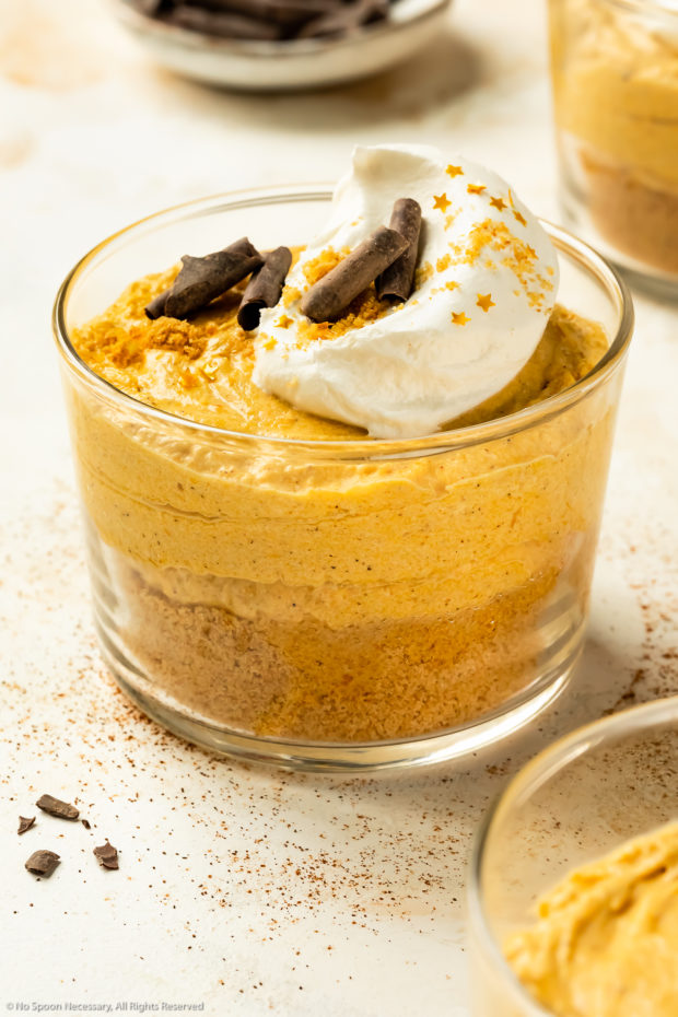 Angled photo of pumpkin mousse topped with whipped cream, chocolate curls and gold flakes in a short dessert glass.