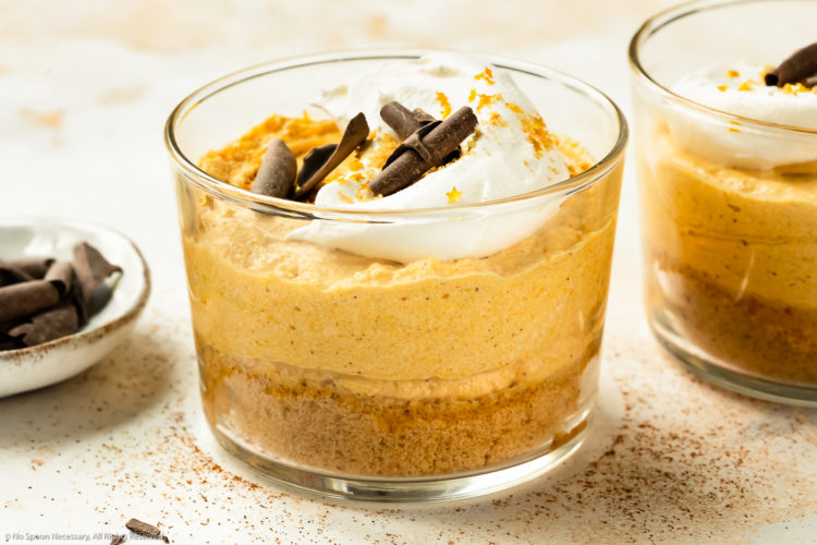 Angled, landscape photo of pumpkin mousse topped with whipped cream, chocolate curls and gold flakes in a short dessert glass.