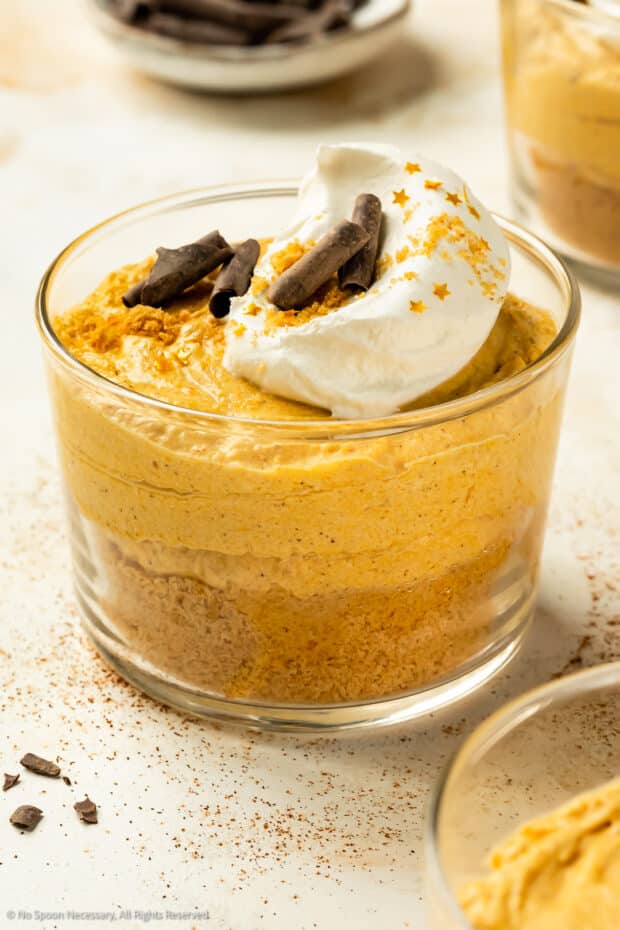 Angled photo of pumpkin mousse topped with whipped cream, chocolate curls and gold flakes in a short dessert glass.