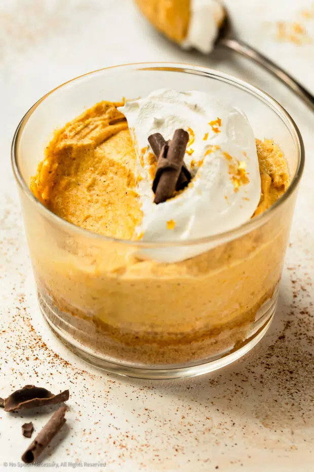 Short dessert glass containing pumpkin mousse with a bite of mousse missing from the dessert.