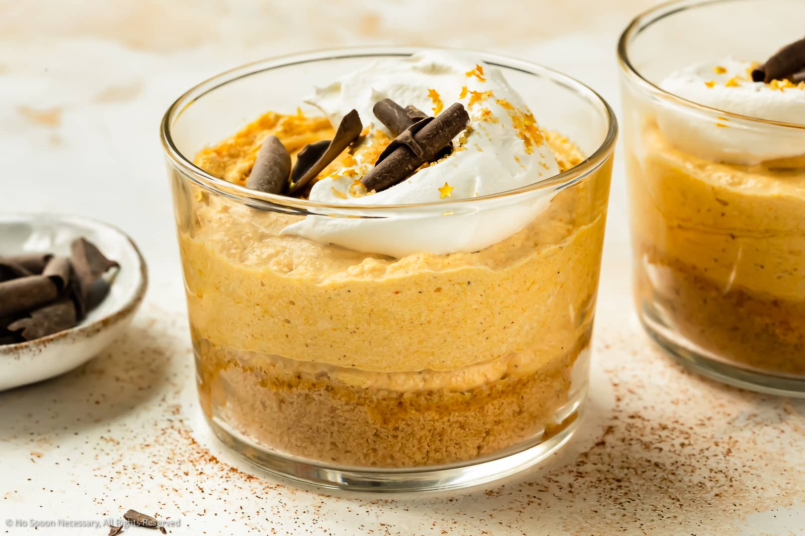 Landscape photo of pumpkin dessert topped with whipped cream, chocolate curls and gold flakes in a short dessert glass.