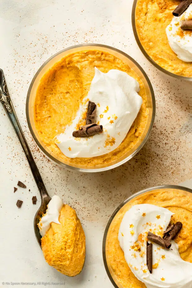 Three short glasses of orange mousse topped with whipped cream and chocolate curls.