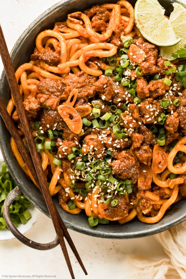Overhead photo of Japanese Pork Udon Stir Fry garnished with sesame seeds and sliced scallions in a small wok with a pair of chopsticks resting on the side of the pan.