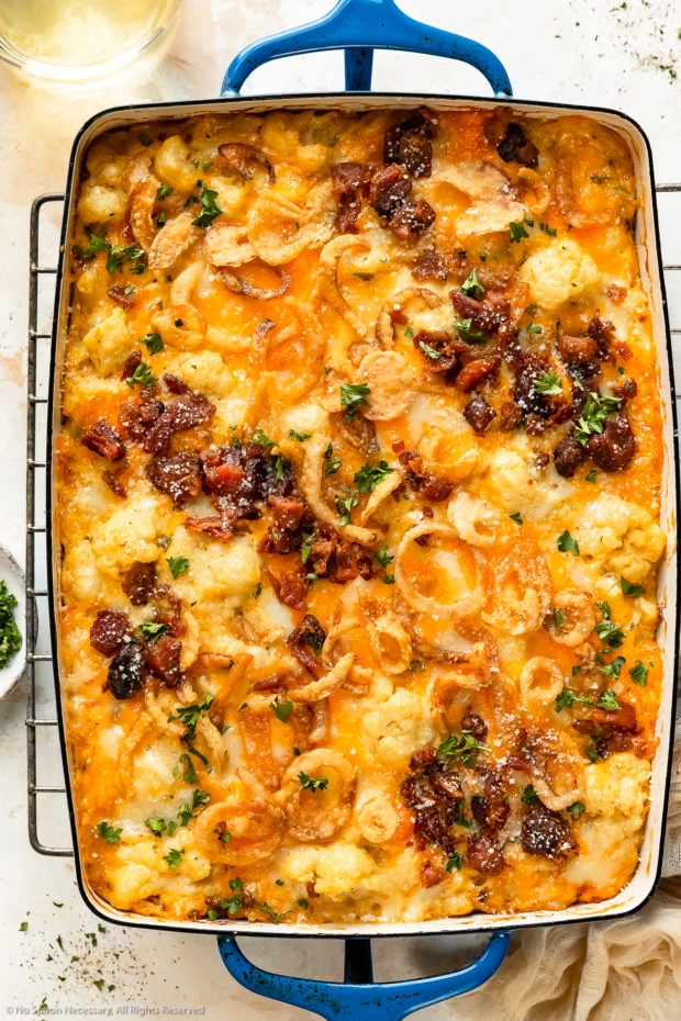 Overhead photo of cheesy cauliflower casserole topped with bacon and crispy onions in a large blue baking dish.