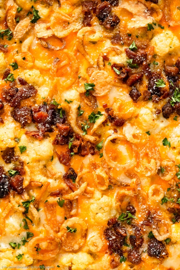 Overhead, close-up photo of the top of cauliflower casserole loaded with cheese, bacon and crispy onions