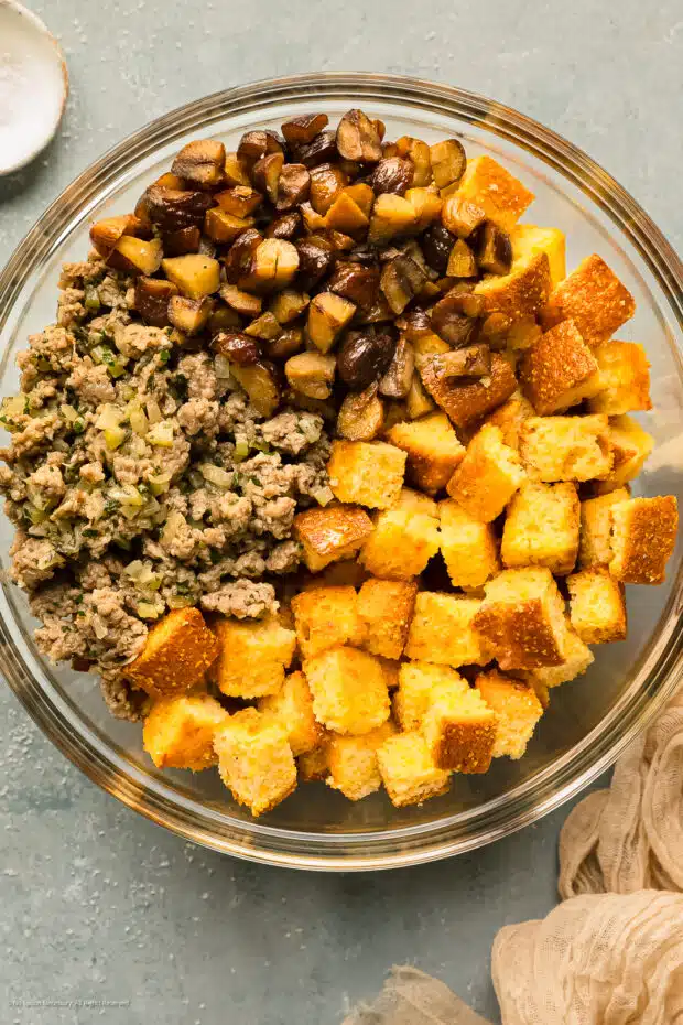 Overhead photo of a mixing bowl filled with chopped chestnuts, cooked sausage and veggies, and toasted cubes of cornbread.