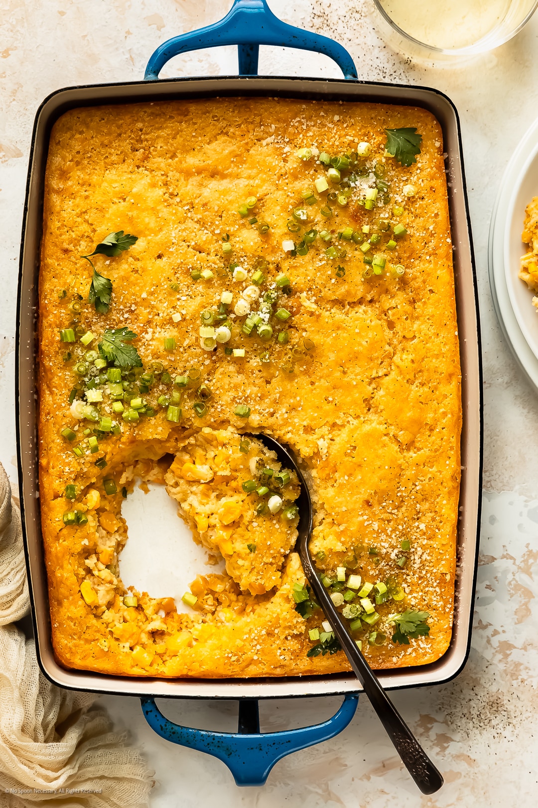 Overhead photo of corn casserole pudding garnished with parmesan and scallions in large baking dish.
