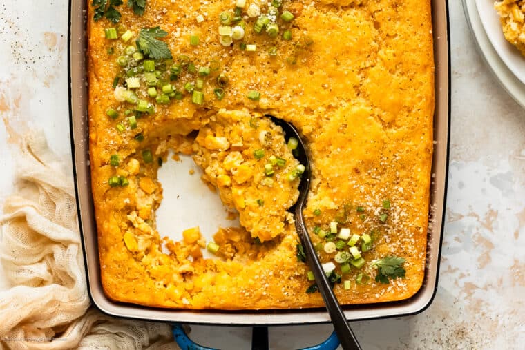 Overhead photo of corn casserole (no jiffy mix) in a blue baking dish with a serving spoon inserted into casserole.