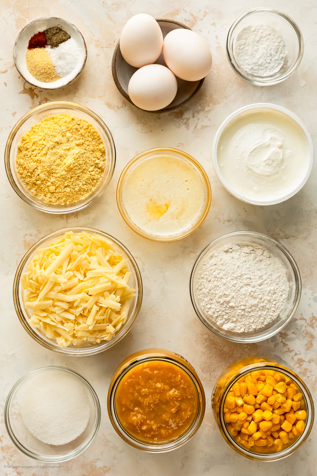 Overhead photo of the eleven ingredients needed to make corn casserole pudding neatly arranged on a kitchen counter.