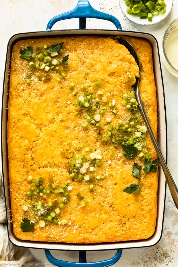 Overhead photo of creamy corn casserole in a blue baking dish with a serving spoon inserted into the casserole.