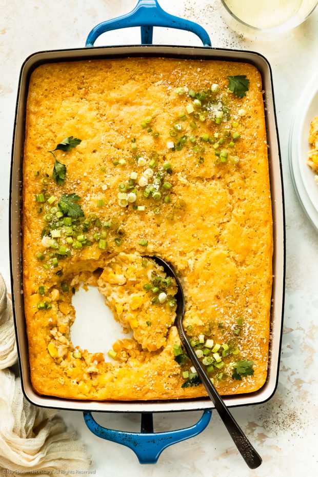 Overhead photo of creamed corn casserole (without jiffy) in a blue baking dish with a serving spoon inserted into the casserole.